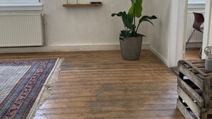 Ein Zimmer mit Holzboden, einem Blumentopf, einem Heizkörper und einem Fenster mit Rollläden.