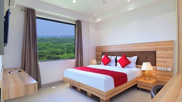 A modern hotel room with a large bed, wooden headboard, and a desk with a chair. - MY HOTEL (New Delhi)