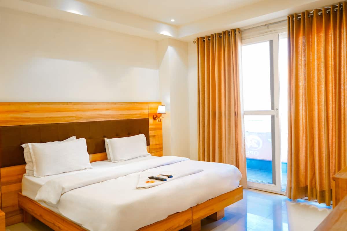 Een hotelkamer met een houten hoofdeinde, een groot bed met witte lakens, een bedlampje en uitzicht op het landschap door een schuifdeur.