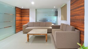 A modern living room with a beige sofa, a wooden coffee table, and a glass partition wall. - MY HOTEL (New Delhi)