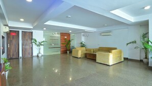 A modern lobby with a polished floor, a sofa, potted plants, and wooden doors. - MY HOTEL (New Delhi)