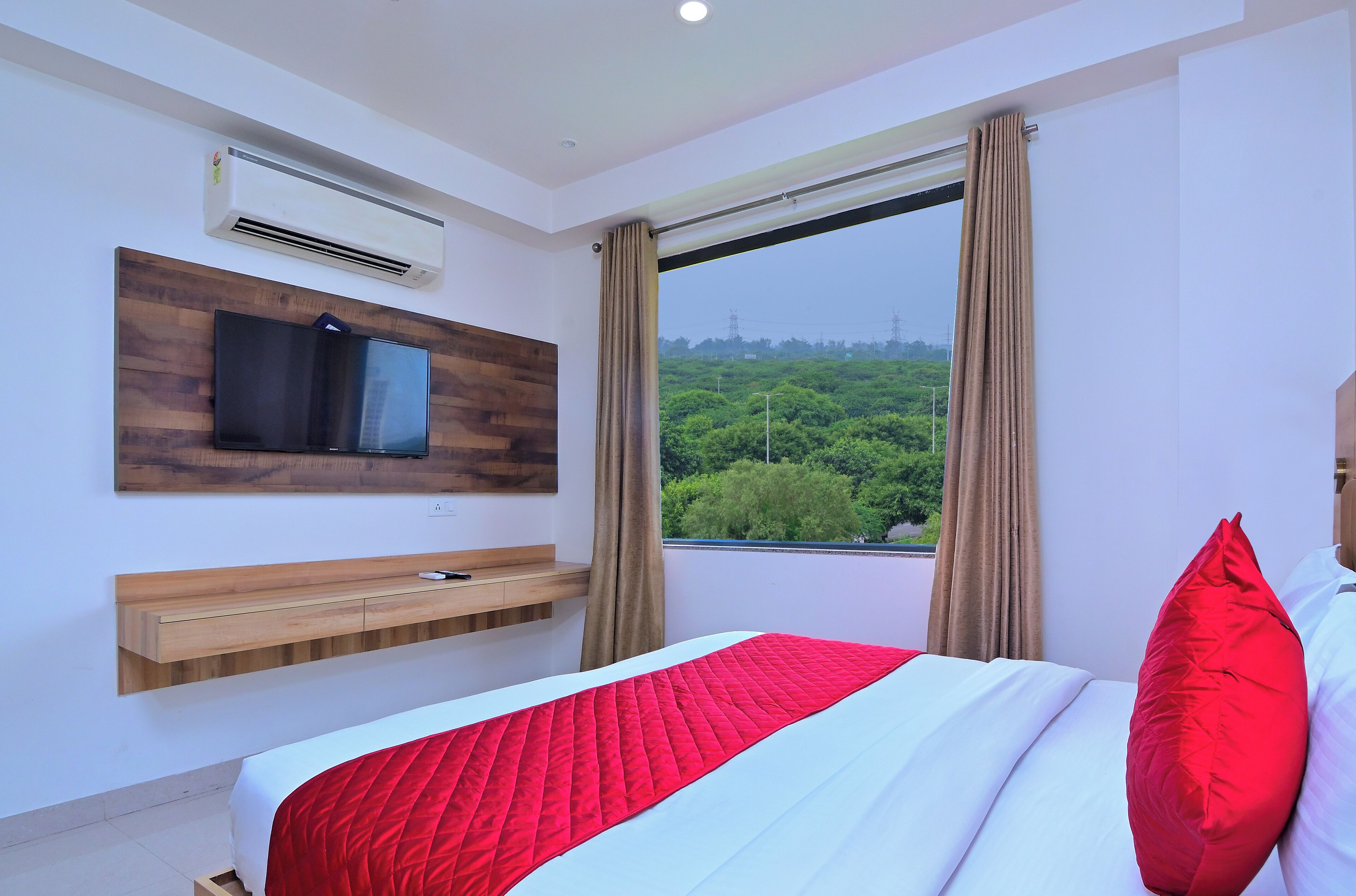 Een moderne hotelkamer met een bed, een wandtelevisie, een houten plank en een groot raam met gordijnen.