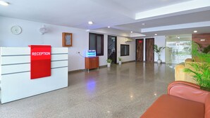 A modern reception area with a reception desk, a clock, and a staircase leading to other floors. - MY HOTEL (New Delhi)