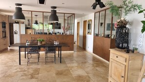 A modern kitchen with a dining area, featuring a large island, dark pendant lights, and a wooden cabinet. - Spacious VILLA 286 m2 overlooking the Sainte Victoire, garden, swimming pool. (Pertuis)