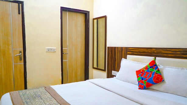 Une chambre d’hôtel avec un lit, une tête de lit en bois, un oreiller coloré et une porte.