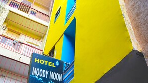Une enseigne d’hôtel portant le nom « MOODY MOON » est fixée à un bâtiment dont les murs extérieurs sont peints en jaune et en bleu.