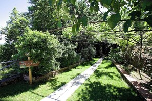 Ein Weg führt durch einen üppigen Garten, ein Schild trägt die Aufschrift 'PARCO RELLA'.