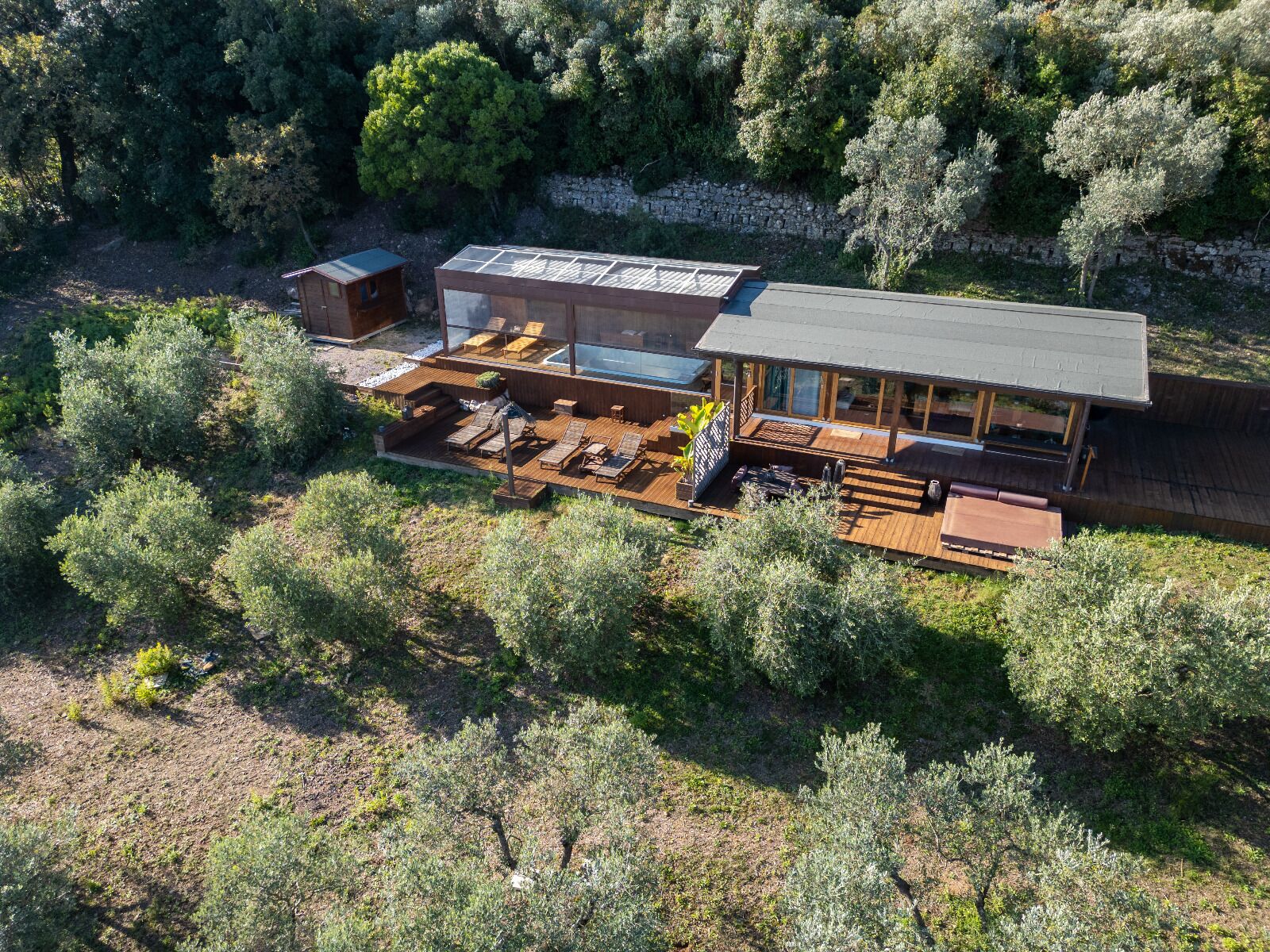 A modern house with a large deck, outdoor seating, and a stone wall.
