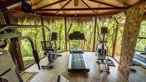 Een overdekte fitnessruimte met loopband, krachtapparaten en een bank.