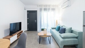 A modern living room with a TV, sofa, coffee table, and a door. - Thalassa-One Bedroom Apartment (Kavala)
