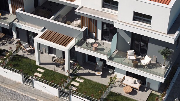 A modern multi-story residential building with balconies, outdoor seating, and a well-maintained garden. - Thalassa-One Bedroom Apartment (Kavala)