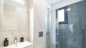 A bathroom with a marble vanity, a shower with a glass door, and a small window. - Thalassa-One Bedroom Apartment (Kavala)