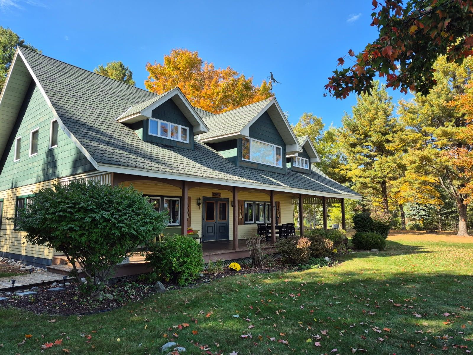 A two-story house with a green roof, a covered porch, and a well-maintained lawn.