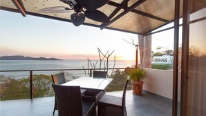 A balcony with a table and chairs, overlooking a body of water and distant land.