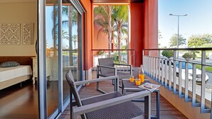 A balcony with a sofa, two chairs, a table with a newspaper and orange juice, and a view of palm trees and a street. - VICTORIA SECRET APARTMENT (Vilamoura)
