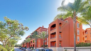 A row of red buildings with balconies, parked cars, and palm trees. - VICTORIA SECRET APARTMENT (Vilamoura)