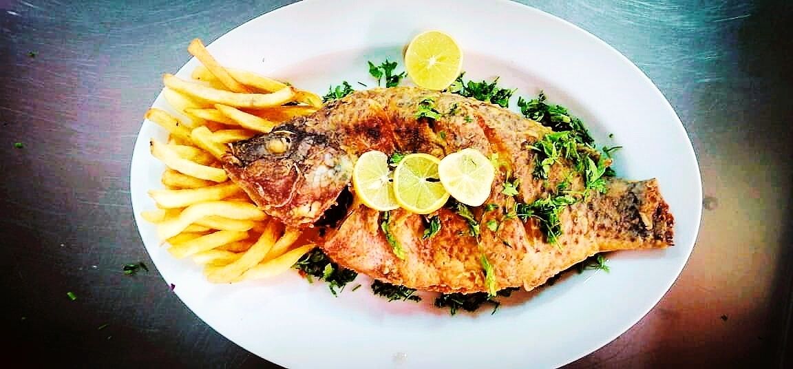 A plate with a whole fish, fries, and lemon slices.