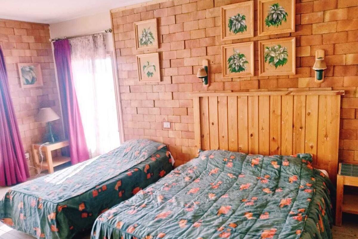 Una habitación con dos camas, cabecero de madera, pared de ladrillo y cuadros enmarcados.