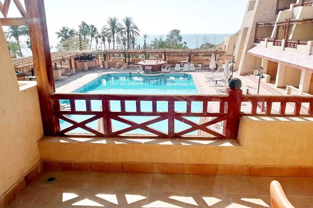 Zona de piscina con vista al mar, una cerca de madera y suelo de baldosas.
