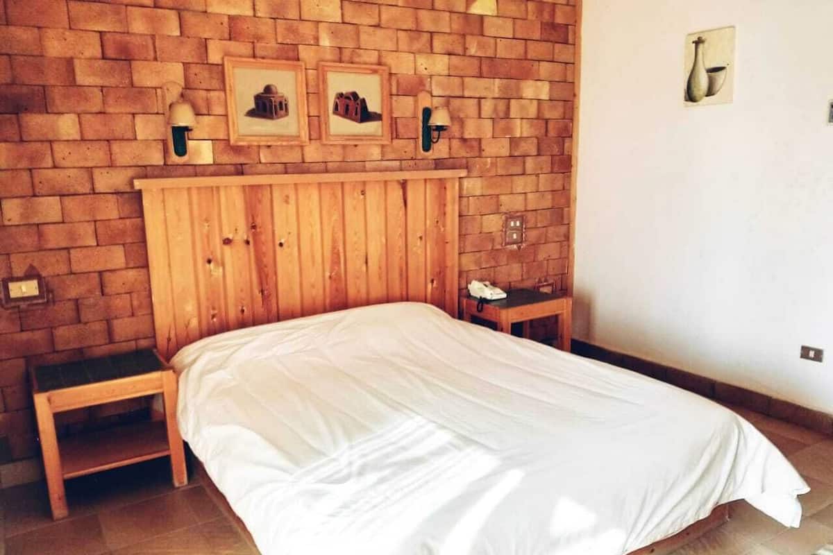 Un dormitorio con cabecera de madera, una cama individual, dos mesitas de noche y una pared de ladrillo con cuadros enmarcados.