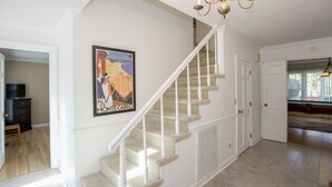 Eine Treppe mit einem Chandelier, einem gerahmten Poster und einer Tür zu einem anderen Raum.
