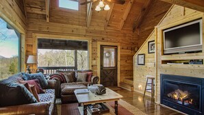 Un intérieur de chalet chaleureux avec une cheminée, des murs en bois, un canapé et un téléviseur.