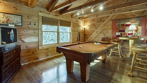 Un intérieur en bois avec une table de billard, un téléviseur et une fenêtre équipée de stores.