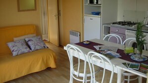 Una habitación compacta con cama, una mesa de comedor, sillas, una pequeña cocina con microondas y refrigerador.