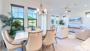 A spacious dining area with a wooden table and chairs, a chandelier, and large windows offering a view of the outdoors. - Two Golf Carts ~ Private Patio ~ Golf Course View (Miramar Beach)