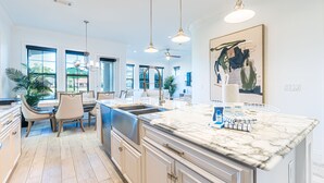 A modern kitchen with a marble countertop, pendant lights, and a dining area with a chandelier. - Two Golf Carts ~ Private Patio ~ Golf Course View (Miramar Beach)