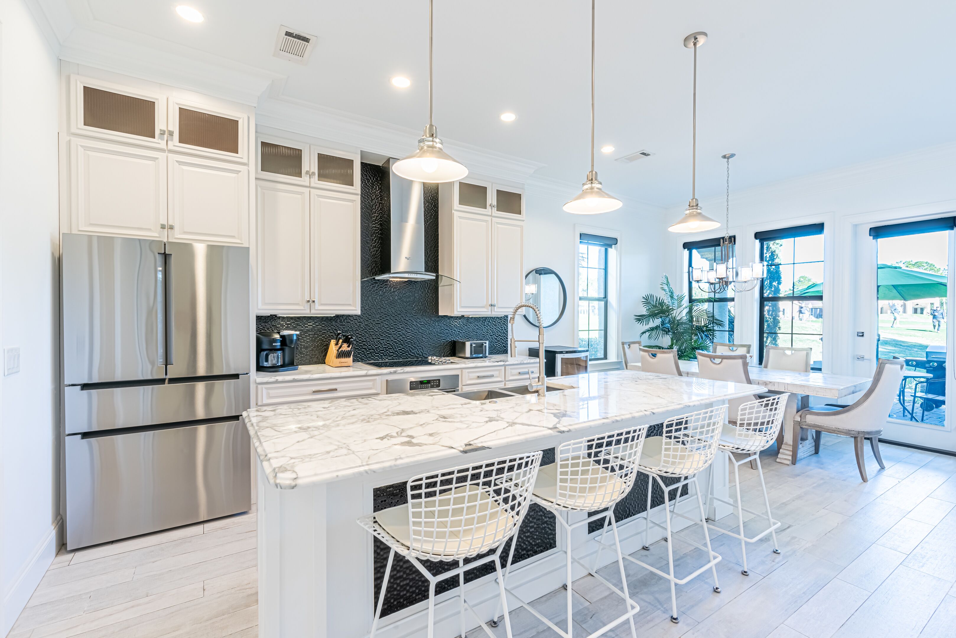 A modern kitchen with white cabinets, stainless steel appliances, and a marble island with bar stools.