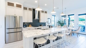 A modern kitchen with white cabinets, stainless steel appliances, and a marble island with bar stools. - Two Golf Carts ~ Private Patio ~ Golf Course View (Miramar Beach)