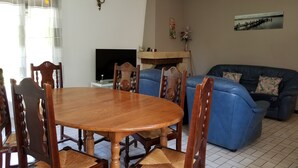 Uma sala de jantar com uma mesa e cadeiras de madeira, um sofá azul, uma TV de tela plana e uma lareira.