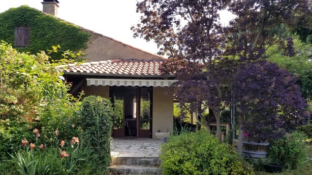 Uma casa com telhado de telhas, varanda coberta e um caminho de pedra que leva à entrada.