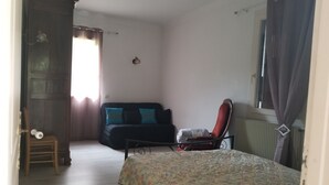 Um quarto com cama, uma cadeira, um sofá, um radiador e uma janela com cortinas.