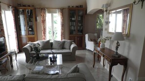 A living room with a sofa, armchair, and a coffee table with decorative items. There are bookshelves and a television in the room. - Beautiful Villa, big pool,  overlooking valley, walking distance to town.  (Seillans)