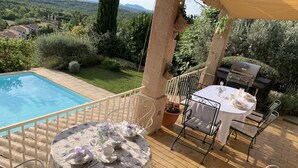A poolside area with a table set for dining, surrounded by metal chairs and a barbecue grill. - Beautiful Villa, big pool,  overlooking valley, walking distance to town.  (Seillans)