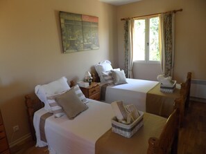 A room with two beds, a wooden table with bread, a window with curtains, and a painting on the wall.
