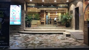 Entrada de hotel con suelo de baldosas de piedra, una mesa de recepción y plantas en macetas.