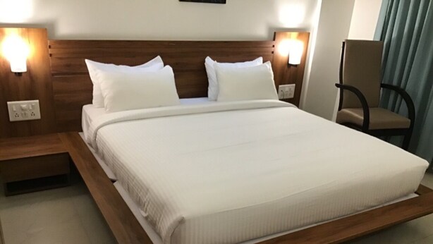 Una habitación de hotel moderna con una cama grande, cabecera de madera, dos mesitas de noche con lámparas y una silla.
