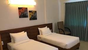Habitación de hotel con dos camas individuales, cabecero de madera, una silla y una obra de arte en la pared.