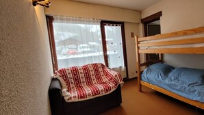 Una habitación pequeña y acogedora con una cama nido, una cama individual, una ventana con cortinas y vistas al exterior.