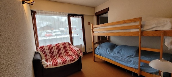 Una habitación pequeña y acogedora con una cama nido, una cama individual, una ventana con cortinas y vistas al exterior.