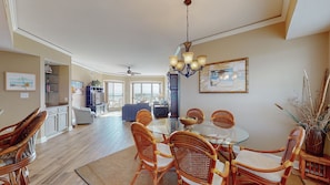 A spacious dining area with a glass table and wicker chairs, a chandelier, and a view to the living area.