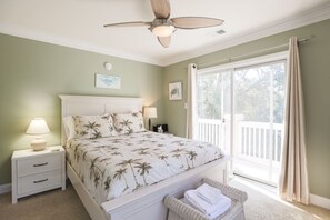 Une chambre à coucher comprenant un lit, des tables de chevet, un ventilateur de plafond, une fenêtre avec des rideaux et une vue sur une terrasse.