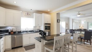 Een moderne keuken met witte kasten, een centraal eiland met stoelen en een eethoek met tafel en stoelen.