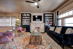 A living room with a fireplace, bookshelves, a sofa, and a coffee table. - 🌿 Boho Glam Bungalow in Historic OKC | 3BR/2BA | Walkable + Central! 🌿 (Oklahoma City)
