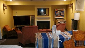 A hotel room with a bed, a TV, a fireplace, a fan, and a table with a lamp. - Basement Studio Apartment (Sanborn)