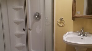 A bathroom with a glass-enclosed shower, a pedestal sink, and a wall-mounted mirror. - Basement Studio Apartment (Sanborn)