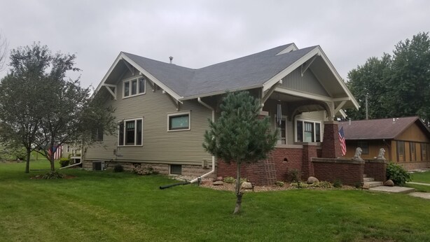 A two-story house with a gabled roof, a front porch, and a small front yard with a tree and a flag. - Basement Studio Apartment (Sanborn)